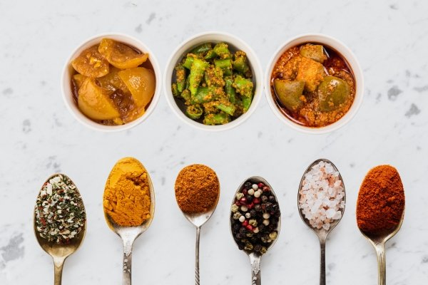Bowls of traditional Indian pickles with assorted spices on spoons – Best Authentic Indian Spices and Pickles Online.