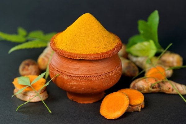 Turmeric powder in a clay pot with fresh turmeric roots and leaves – why turmeric powder is good for skin.