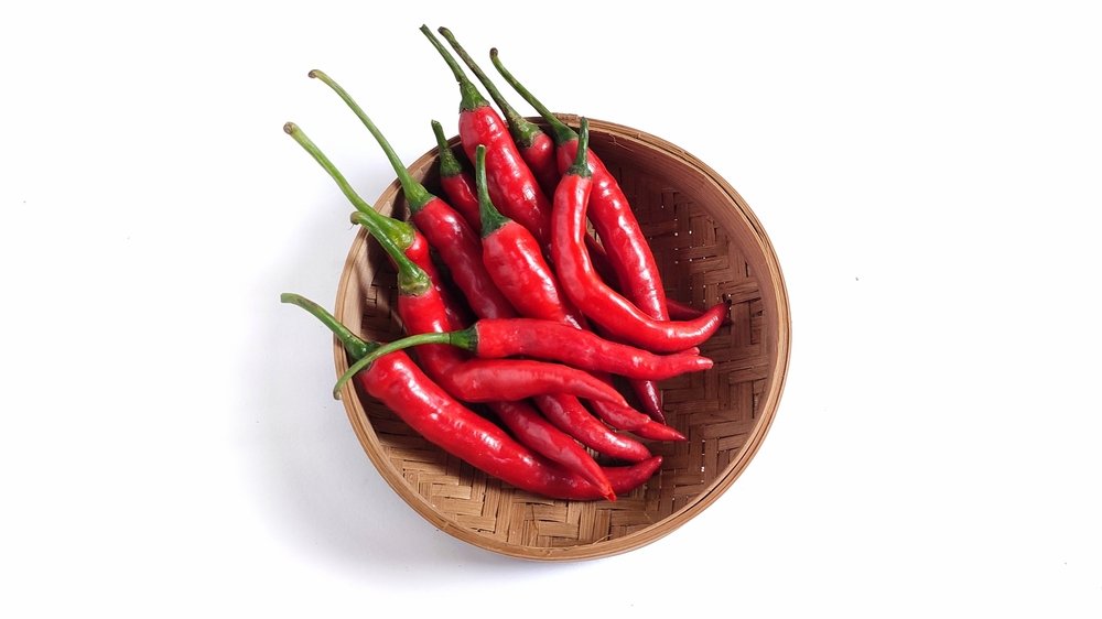 Fresh red chillies in a brown wooden bowl placed on a rustic surface.